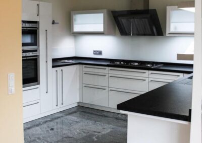 Moderne Küche in Weißlack mit Edelstahlstangengriffen. Die Arbeitsplatte ist aus schwarzem Granit. Eine Besonderheit ist die untergebaute Edelstahlspüle mit eingefräßter Abtropffläche in Granit.